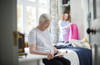 elderly woman sitting n bed with care worker in background