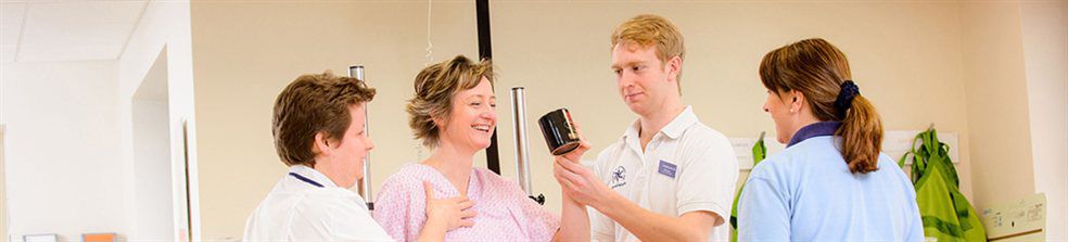 Three medical staff assisting a woman to hold up a mug