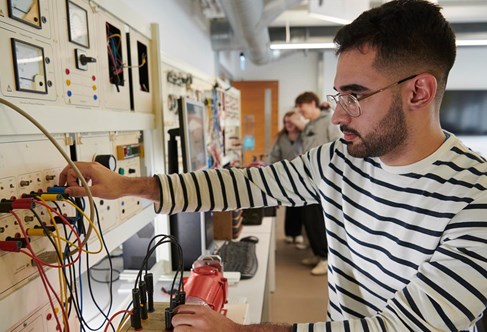 Student standing in front of electrical engineering test equipment with cables
